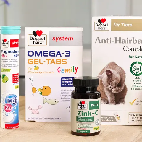 Die Abbildung zeigt verschiedene Gesundheitsprodukte auf einem Holztisch. Darunter befinden sich Magnesium, Omega-3 Gel-Tabs, ein Anti-Haarball-Komplex für Katzen, Zink+C Kapseln und Vitamin D3 Tropfen. Alle Produkte gehören zur Marke Doppelherz.