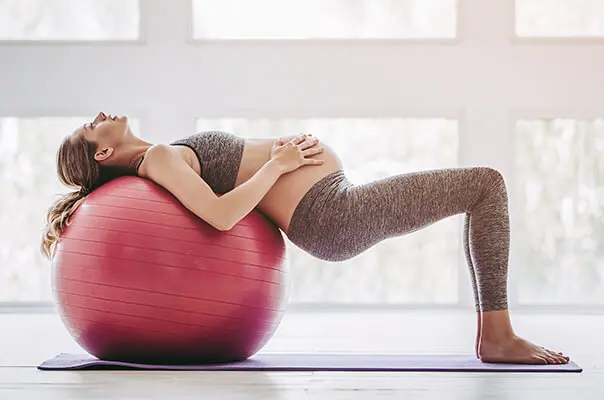 Schwangere Frau liegt auf Gymnastikball