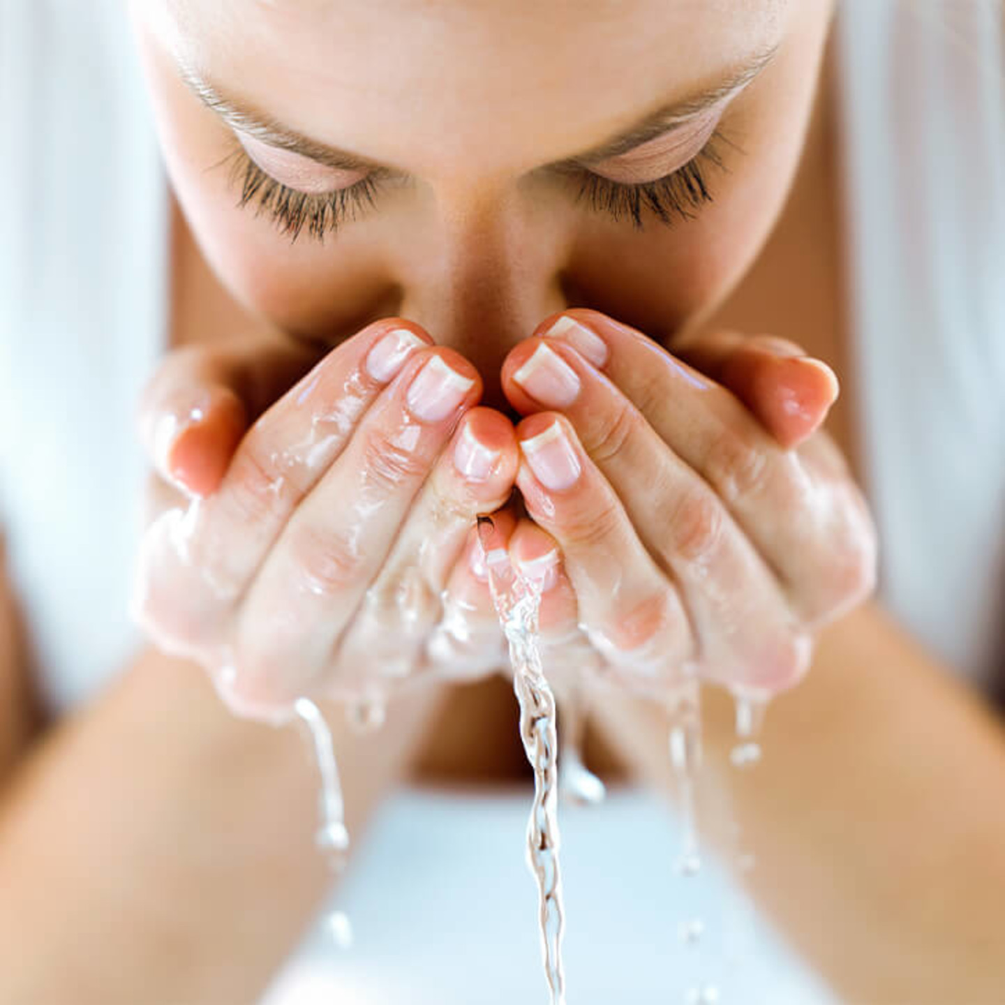 Frau spritzt sich Wasser ins Gesicht: Hylauronsäure bindet Wasser im Körper.