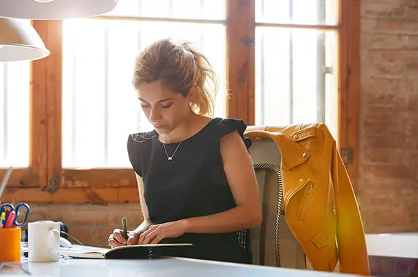 Frau schreibt in Notizbuch am Schreibtisch
