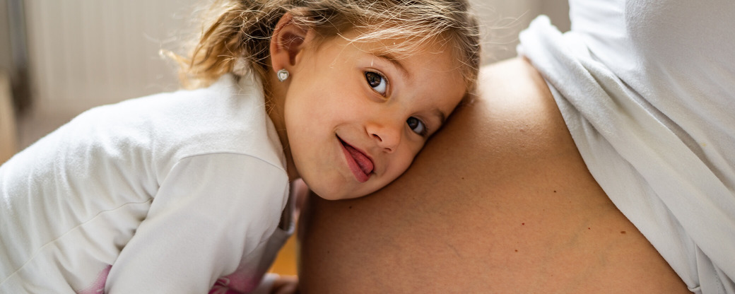 Tochter legt Kopf auf Babybauch der Mutter